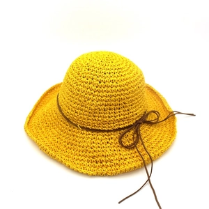 Detailed close-up of yellow raffia sun hat featuring hand-woven texture and brown leather bow