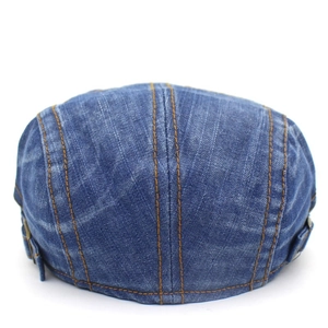 Close-up of washed denim flat cap showing orange stitching and side metal buckle