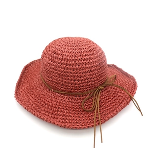 Close-up of rust red raffia sun hat featuring a wide wavy brim and delicate bow ribbon