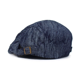 Detail of adjustable metal buckle and dark blue textured denim fabric on back of beret