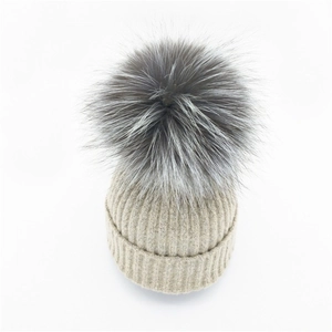 Beige gerippte Strickmütze mit einem flauschigen grauen Kunstfellbommel für den Winter