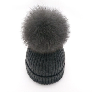 Detail of dark grey knit beanie featuring a fluffy fox fur pom-pom and ribbed texture