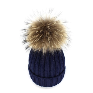 Macro detail of navy blue ribbed knit texture and large faux fur pompom on beanie