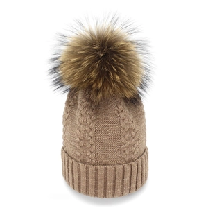 Detailed cable knit texture of a khaki winter hat with a large fluffy pom-pom
