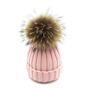 Detailed texture of pink ribbed knit beanie featuring a large fluffy faux fur pom-pom