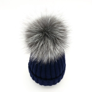 Close-up of navy blue ribbed knit beanie with a fluffy grey faux fur pompom detail