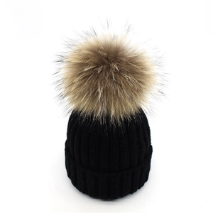 Close-up of black ribbed knit beanie featuring a fluffy natural raccoon fur pompom detail