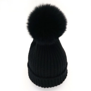 Close-up of black ribbed knit beanie featuring a large fluffy faux fox fur pompom top
