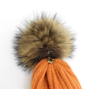 Detail of orange knit beanie with detachable natural fur pompom and metal snap button