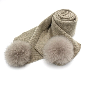Cozy beige knitted winter scarf featuring two fluffy fox fur pom-poms on a white background