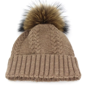 Close-up of winter knit beanie showing cable pattern and large fluffy faux fur pompom