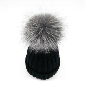 Close-up of thick black ribbed knit beanie with a fluffy grey silver fox fur pom-pom