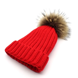 Detailed view of red knitted beanie with thick ribbing and a large faux fur pom-pom