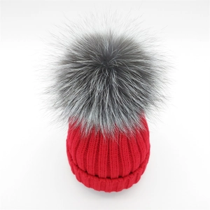 Detailed close-up of thick red knit pattern and fluffy fox fur pom-pom on winter beanie