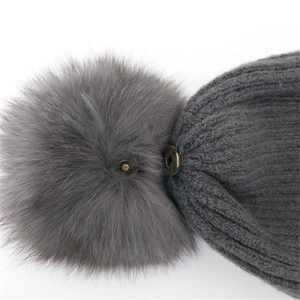 Grey knit beanie with detachable pom-pom featuring a secure metal snap button detail