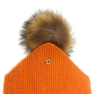 Orange knit beanie with detachable brown fur pom-pom showing the metal snap button detail