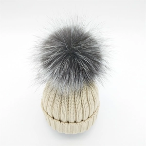 Detail of chunky ribbed knit winter beanie featuring a large fluffy silver fox fur pompom