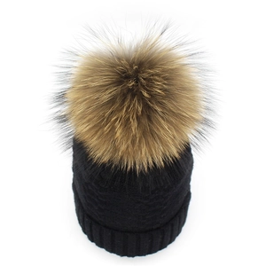 Close-up of black cable knit winter hat with a large fluffy brown faux fur pom-pom