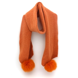 Detail of bright orange knitted winter scarf featuring soft matching faux fur pom-poms