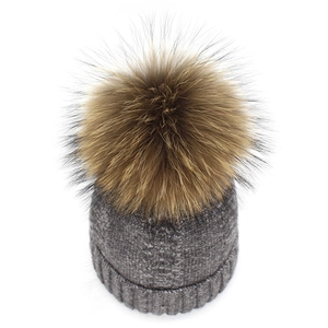 Macro detail of grey cable knit texture and fluffy raccoon fur pom-pom on beanie hat
