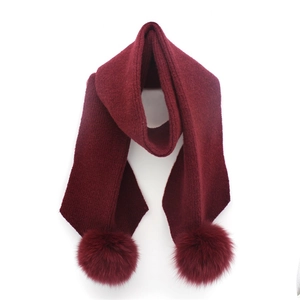 Detailed view of burgundy knit wool scarf featuring large fox fur decorative pompoms