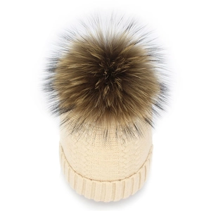 Detail of beige knit beanie with classic cable pattern and large fluffy faux fur pompom