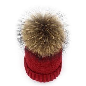 Close-up of a deep red knit beanie featuring a large fluffy brown pom-pom for winter wear