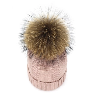 Close-up of pink cable-knit beanie with fluffy brown raccoon fur pom-pom detail