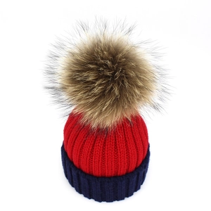 Detailed close-up of a two-tone red and navy blue knit beanie with a fluffy fur pom-pom