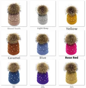 Grid display of nine colored pearl knitted hats with large faux fur pom poms on top