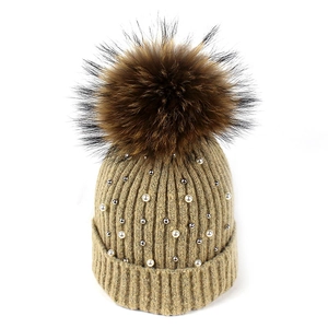 Detail of knitted winter beanie featuring elegant white pearls and a fluffy faux fur pompom