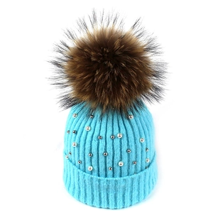 Detail of light blue knit hat with white pearls, metal studs, and a fluffy fur pom-pom