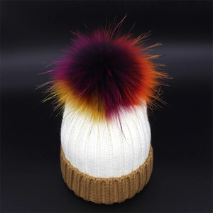 Close-up of knit white beanie with brown ribbed cuff and a colorful large pom-pom detail