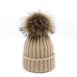 Detailed view of the thick-ribbed knit pattern and large fluffy fur pompom on this beige beanie