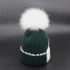 Dark green knitted beanie featuring a white fox fur pompom and wavy stitch patterns