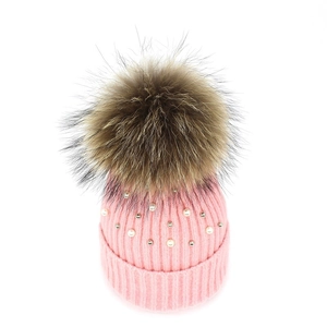 Detail of pink ribbed knit beanie featuring faux pearls and a large fluffy fur pompom