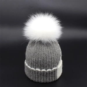 Detail of grey knit beanie with white fluffy fur pom-pom and contrast stitching