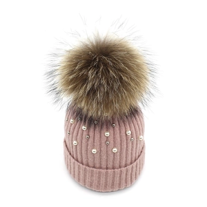 Close-up of pink knit hat featuring faux fur pompom and white pearl embellishments