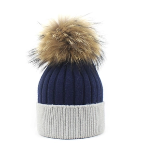 Detailed knit texture of a two-tone winter beanie with a fluffy fur pom-pom on top