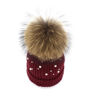 Detail of burgundy knit beanie with white pearls and large natural fur pompom decoration