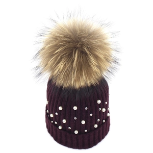 Detail of dark purple knit hat featuring white pearls and a large fluffy fur pompom