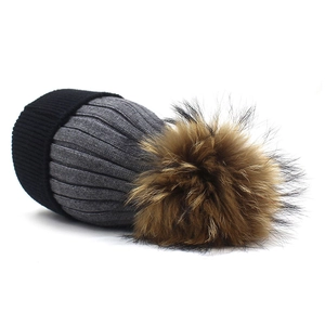 Detailed close-up of a two-tone knit cashmere hat with a large fluffy raccoon fur pom-pom