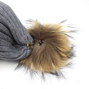 Detail showing the metal snap button for the detachable raccoon fur pompom on grey hat