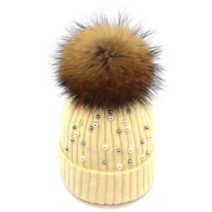 Detailed texture of beige ribbed knit hat with white pearls and a fluffy brown pom pom