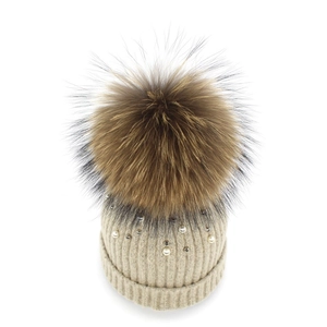 Detailed close-up of beige knit beanie featuring white pearls and a fluffy fur pom-pom