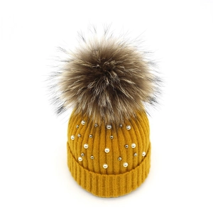 Detailed knit texture of a yellow winter beanie with white pearls and a large faux fur pompom