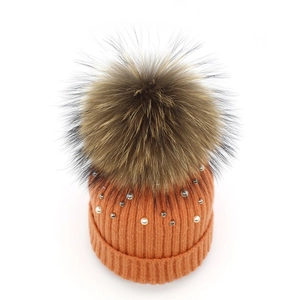 Detail of orange knit beanie with white pearls, silver beads and large fur pompom