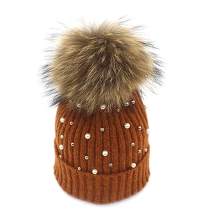 Detail of caramel knit beanie featuring fluffy fur pompom and pearl bead embellishments