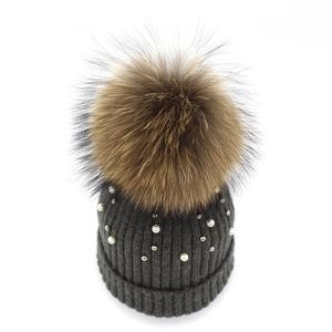 Detail of dark grey knit beanie with fluffy fur pompom and delicate faux pearls