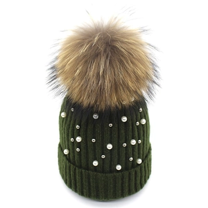 Detailed close-up of dark green knitted hat featuring white pearls and large fur pompom